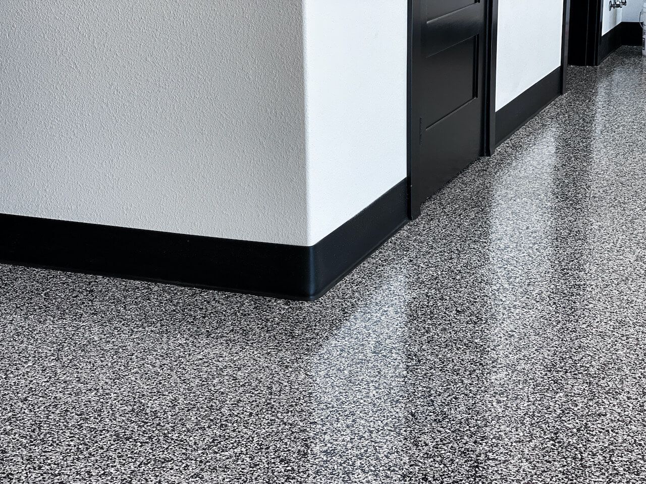 Industrial-grade black and white epoxy flake floor installed in a modern garage.  This garage features black doors and black trim that match the floor.