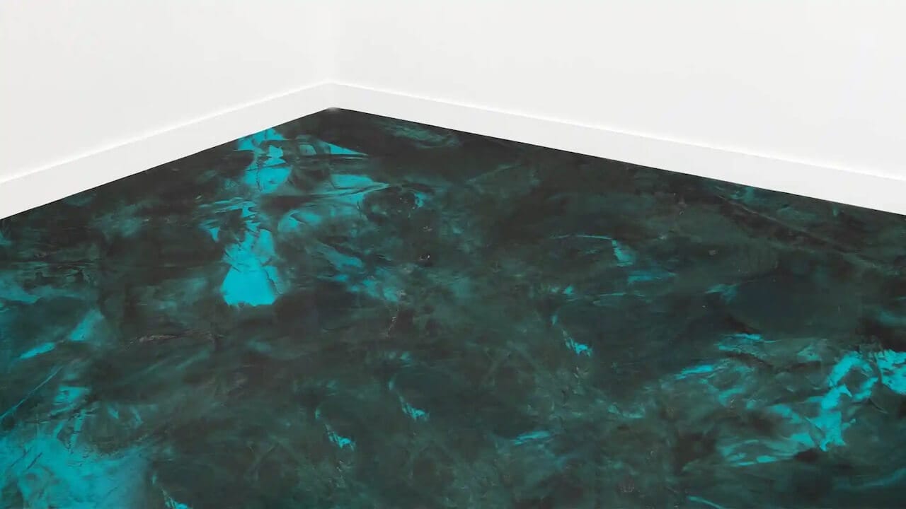 This metallic epoxy floor features a black base coat with turquoise highlights.  This space also features white walls and white trim.